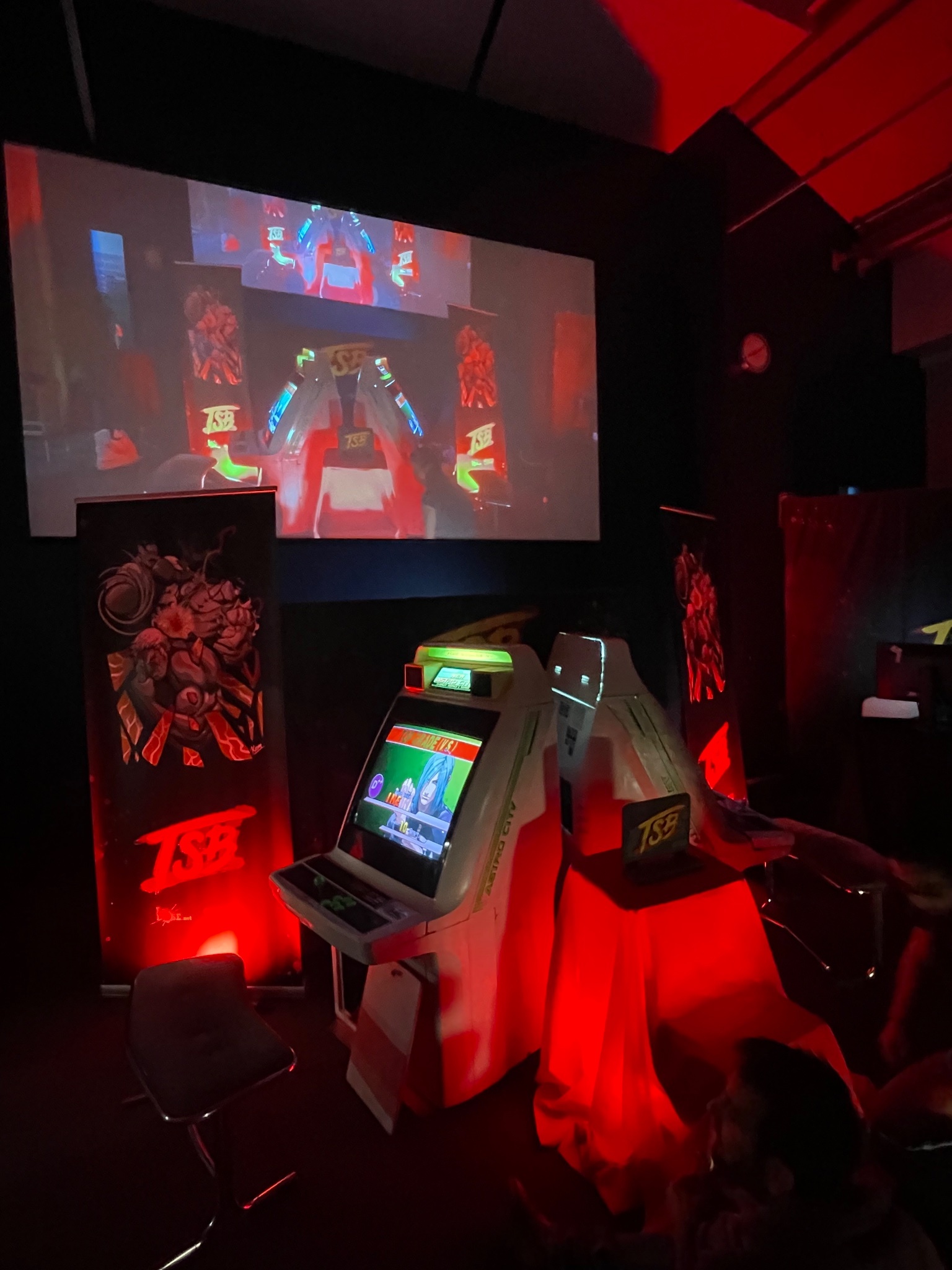 Two arcade cabs under a movie screen. There are decorations and a red light.